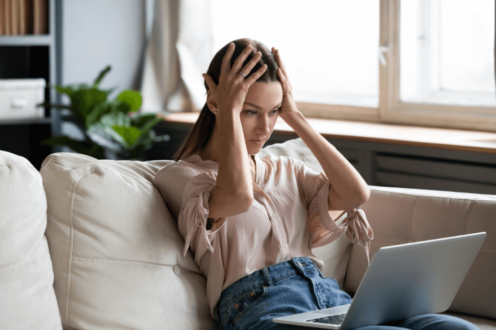 woman sitting on couch looking frustrated at laptop