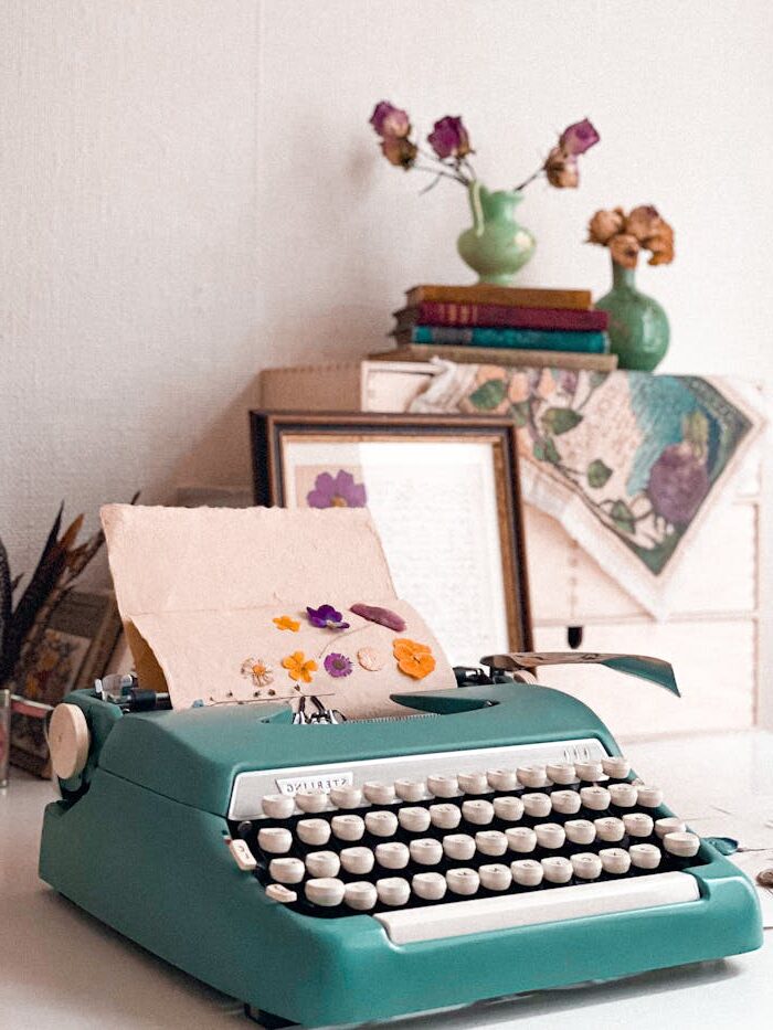 photo of teal-colored typewriter on a desk with plants and artwork